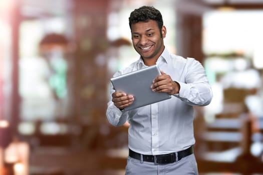 Joyful young businessman playing game on digital tablet pc. Blur interior background.