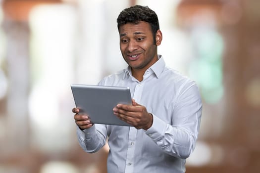 Young surprised businessman looking at digital tablet pc. Man using computer tablet on abstract bokeh background.