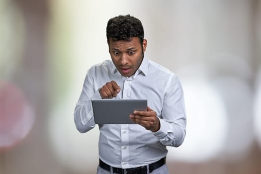 Surprised young businessman looking at digital tablet pc. Abstract bokeh background.
