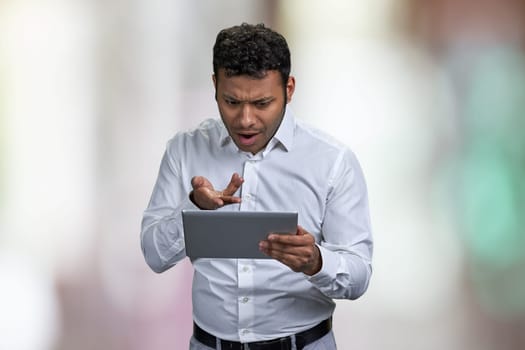 Shocked young businessman looking at digital tablet pc. Surprised man with computer tablet on abstract bokeh background.
