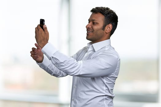 Handsome Indian man taking photo with mobile phone. Young man having video call with smartphone.