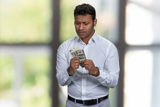 Portrait of handcuffed Indian man holding money. Blur interior background. Corruptibility concept.