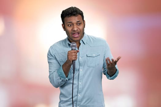 Young handsome man entertainer talking into microphone. Abstract pink bokeh background.