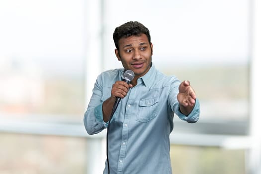 Young handsome man wearing blue shirt speaking to microphone pointing with index finger to the side. Entertainment concept.