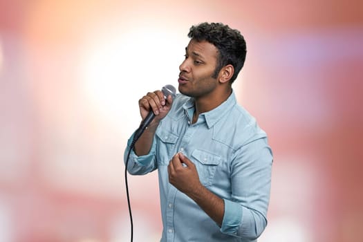 Young indian man performing lyric song on abstract pink bokeh background. People, music, leisure and performance concept.