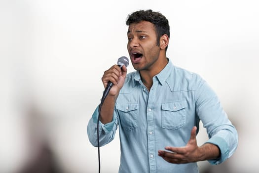 Young indian man performing song into microphone on blurred background. People, music and leisure concept.