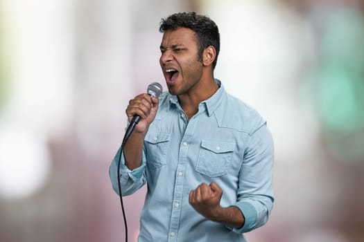 Passionate male singer performing favorite song. Abstract bokeh background. Handsome man singing with passion.