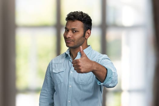 Handsome young man looking at camera and giving thumb up gesture. Attractive indian guy showing thumb up symbol.