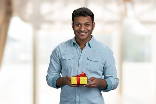 Handsome smiling man holding gift box and looking at camera. Birthday present for her.