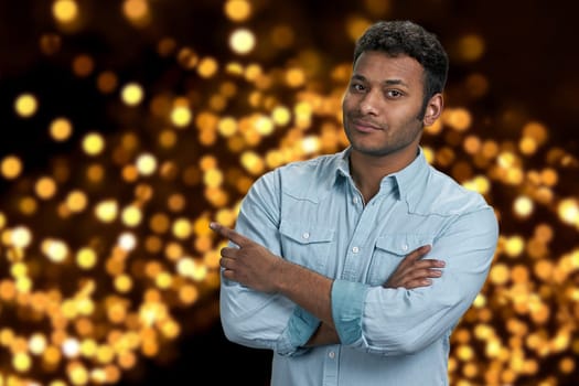 Handsome young man pointing with finger aside. Festive bokeh lights background. Christmas holiday deal.