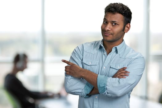 Handsome Indian businessman pointing at copy space. Office interior blur background. Product advertisement concept.