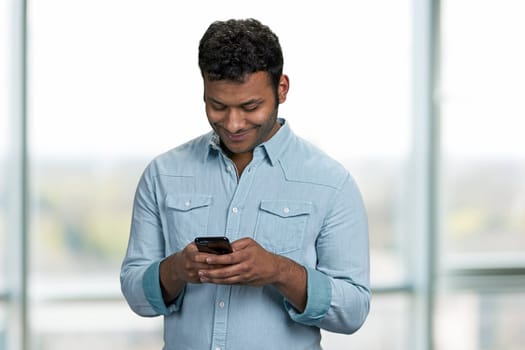 Young smiling man texting message on his cell phone. People, technology and internet communication concept.