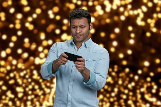 Handsome indian man playing game on mobile phone. Festive bokeh lights in the background.