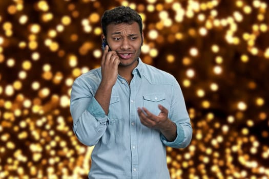 Young handsome man wearing blue shirt talking on mobile phone. Festive bokeh lights in the background.