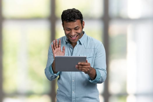 Smiling young man waving with hand while doing video call through digital tablet. Communication via internet.