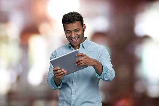 Cheerful young man playing game on digital tablet. Interior blur background.