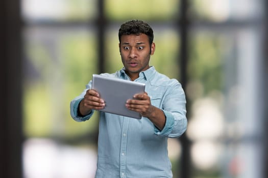 Surprised indian man using digital tablet pc. Interior blur background.