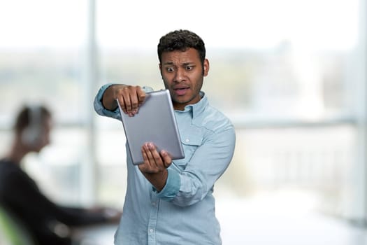 Ecstatic young man playing game on digital tablet. Office interior blur background.