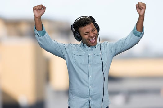 Energetic young man listening to music with headphones and raised his hands. Positive emotions from listening of favorite song.
