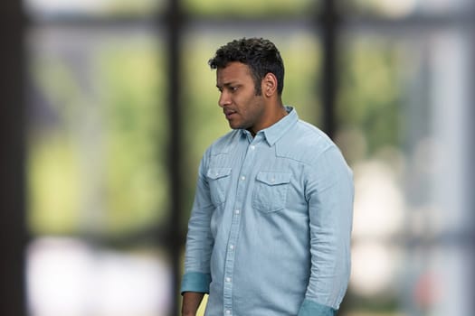 Side view of young sad pensive man on interior blur background. People, emotions and expressions concept.