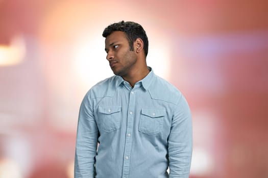 Upset young indian man on abstract pink bokeh background. People, emotions and facial expressions concept.