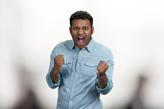 Emotional young man clenched fists and screaming in aggression. Furious indian man on blurred background.
