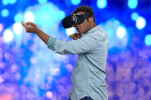 Young man wearing virtual reality glasses. Blue bokeh lights background. Shooting VR game.