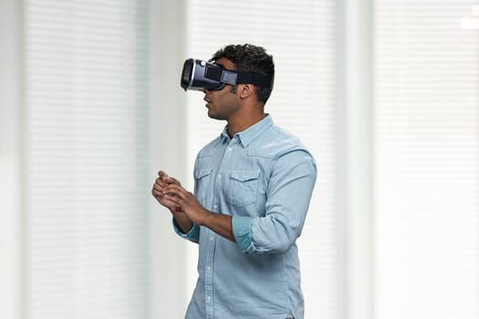 Indian man with VR goggles experiencing VR game. People, technology and fun concept.