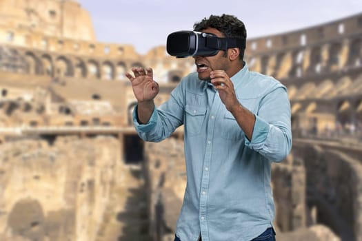 Young handsome guy wearing vr glasses. Blurred background of Colosseum at Rome, Italy. People, technology and travel concept.