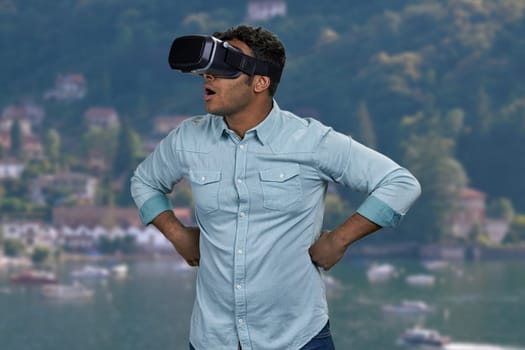 Surprised young man wearing virtual reality glasses. Blur sea and mountains in the background.