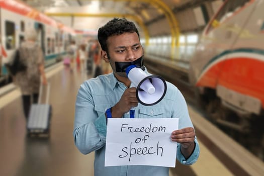 Man with taped mouth holding megaphone. Blurred metro subway station background. Freedom of speech.