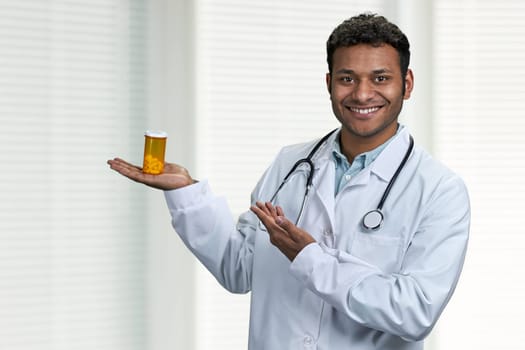 Young indian doctor with stethoscope presenting pills on blurred clinic background. Medicine and healthcare concept.