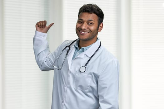 Smiling male doctor with stethoscope pointing with finger at copy space. Place for advertisement.