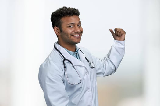 Young handsome doctor with stethoscope pointing aside with finger. Product advertisement concept.