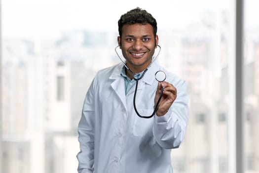 Smiling male doctor looking at camera and showing stethoscope. People, medicine and lifestyle concept.