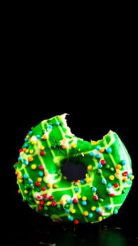 Green glazed donut with sprinkles isolated. Close up of colorful bitten donut.