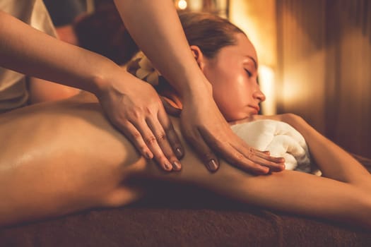 Caucasian couple customer enjoying relaxing anti-stress spa massage and pampering with beauty skin recreation leisure in warm candle lighting ambient salon spa at luxury resort or hotel. Quiescent