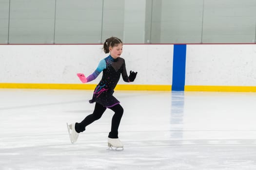 Young girl perfecting her figure skating routine while wearing her competition dress at an indoor ice rink.