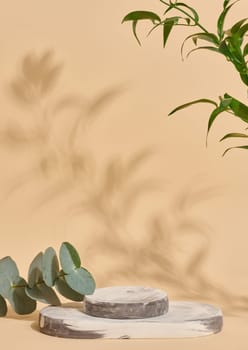 Empty  white marble stand on a beige background and green leaves, a place to display cosmetics and products