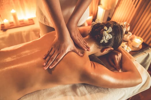 Caucasian woman customer enjoying relaxing anti-stress spa massage and pampering with beauty skin recreation leisure in warm candle lighting ambient salon spa at luxury resort or hotel. Quiescent