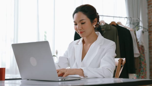Young businesswoman sitting on the workspace desk using laptop computer for internet online content writing or remote working from home. Clothing and textile business marketing analysis. Vivancy