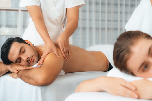 Caucasian couple customer enjoying relaxing anti-stress spa massage and pampering with beauty skin recreation leisure in day light ambient salon spa at luxury resort or hotel. Quiescent