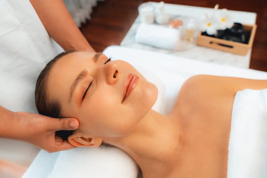 Caucasian woman enjoying relaxing anti-stress head massage and pampering facial beauty skin recreation leisure in dayspa modern light ambient at luxury resort or hotel spa salon. Quiescent