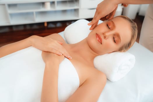 Caucasian woman enjoying relaxing anti-stress head massage and pampering facial beauty skin recreation leisure in dayspa modern light ambient at luxury resort or hotel spa salon. Quiescent