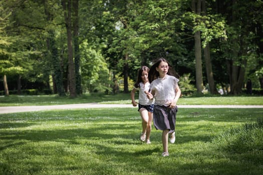 Two beautiful Caucasian brunette girls play happily while running catch up on a summer day in a public park, close-up side view.