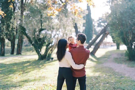 Little girl in the arms of her father, who is hugged by her mother. Back view. High quality photo