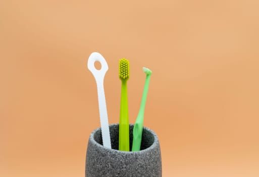 Personal Dental Oral Hygiene Set. Green Toothbrush, White Flexible Tongue Scraper, Interdental Toothbrush For Cleaning Between Teeth On Peach Yellow Background. Space For Text. Horizontal Plane