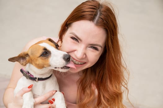 Dog jack russell terrier licks the owner in the face outdoors. Girl with braces on her teeth