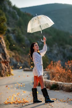 woman umbrella leaves , She holds him over her head, autumn leaves are falling out of him. Beautiful woman in a dress with an umbrella in the autumn park on the road in the mountains