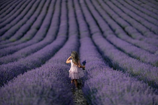 Lavender field girl. Back view happy girl in pink dress with flowing hair runs through a lilac field of lavender. Aromatherapy travel.